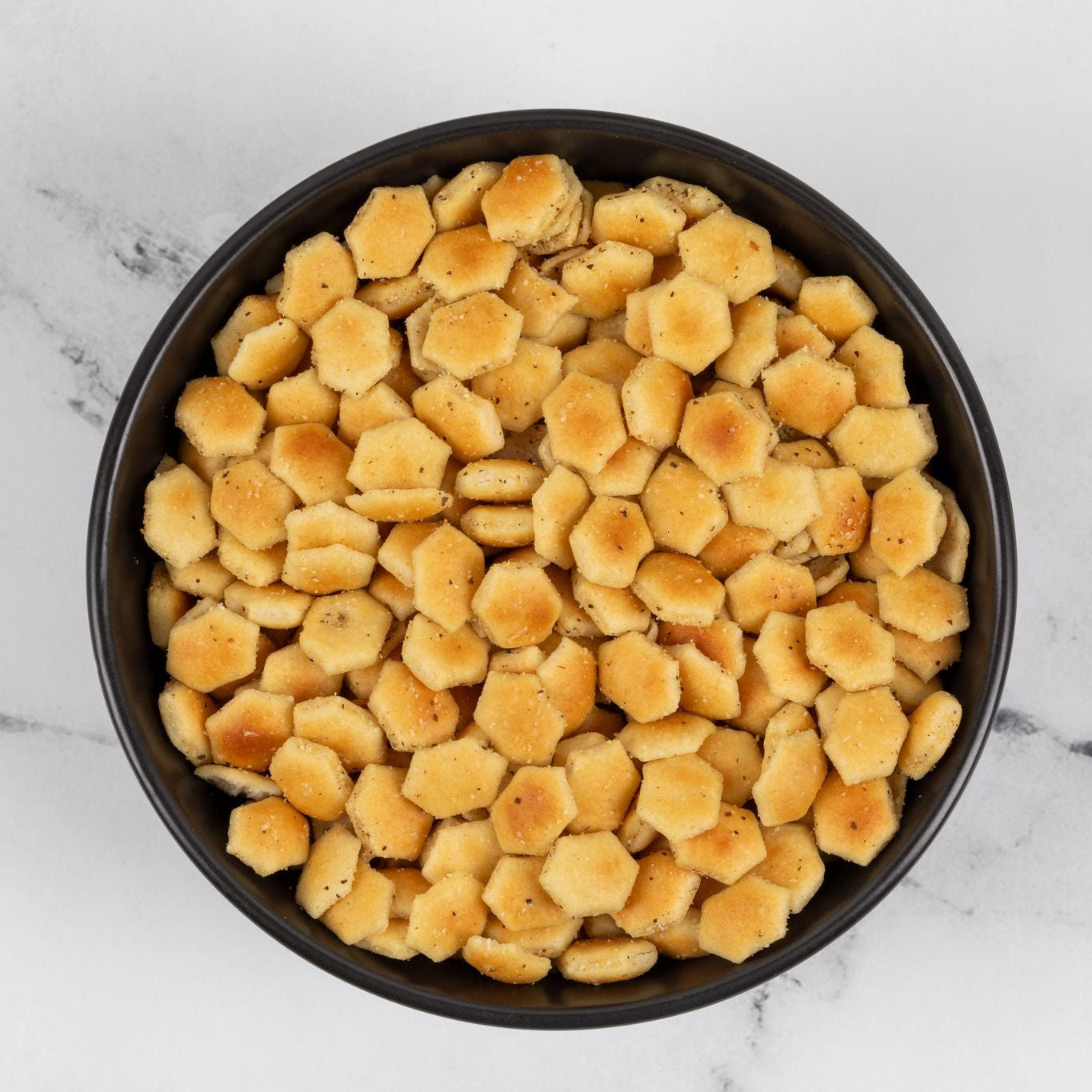 Black bowl filled with oyster crackers on a marble surface