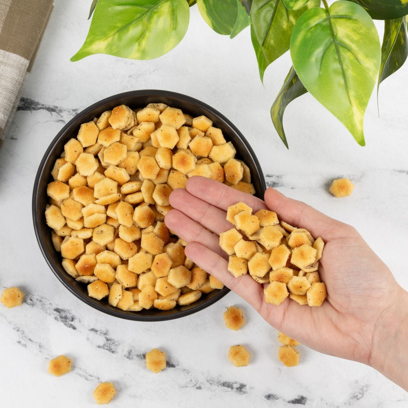 Hand holding yellow snack balls over a bowl with a marble background